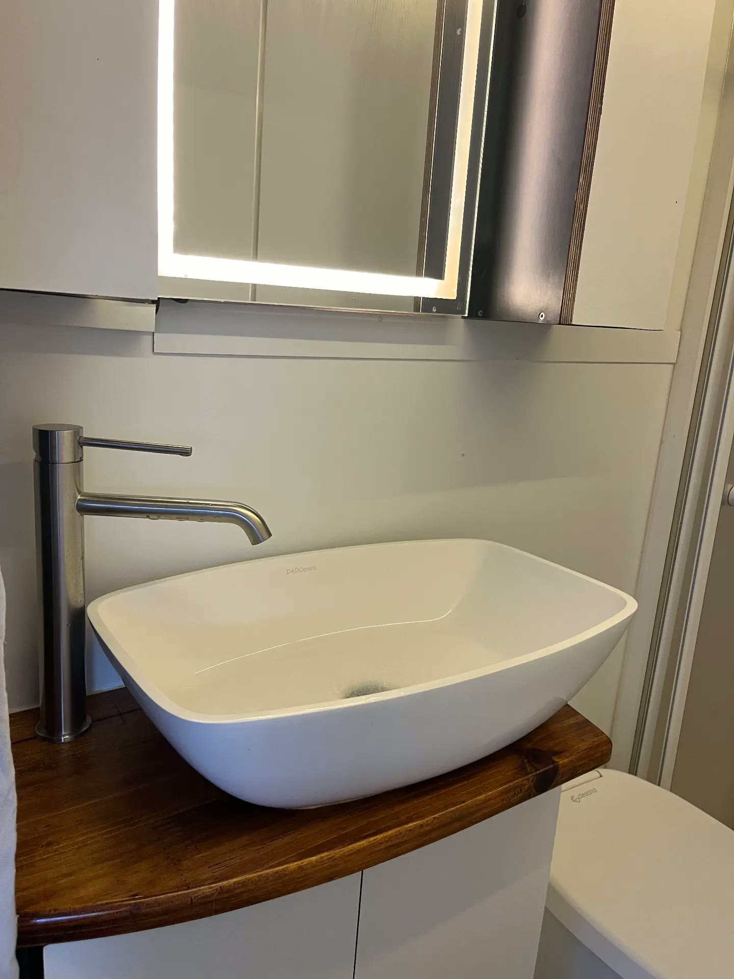 Waschbecken mit Holzablage und beleuchtetem Spiegel